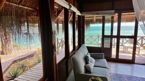 Una habitación con paredes de madera, un sofá, una mesita con una planta y vistas a la playa y al océano a través de amplios ventanales.