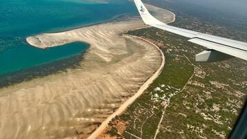 Vista aérea de una zona costera con playa de arena, aguas azules cristalinas y una combinación de vegetación verde y desarrollo urbano.