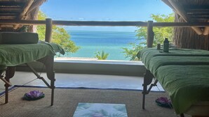 Una habitación con dos camas, techo de paja y vista al océano.