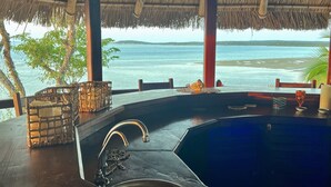 Un área de piscina con techo de paja, un lavabo y vista al océano.