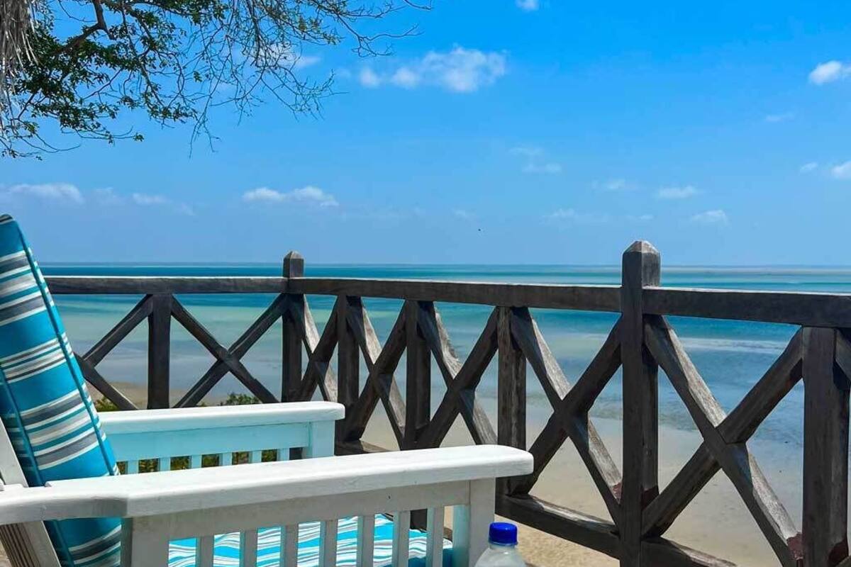 A deck with a view of the ocean, a chair with striped cushions, a bottle of water, and a tray with lemons and mint leaves.