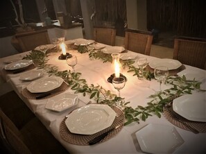 A dining table set with white plates, glasses, and a candle centerpiece, surrounded by wicker chairs. - Moyeni Lodge (Vilanculos)