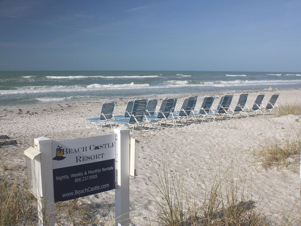 A beach resort sign with a row of beach chairs and the ocean in the background.