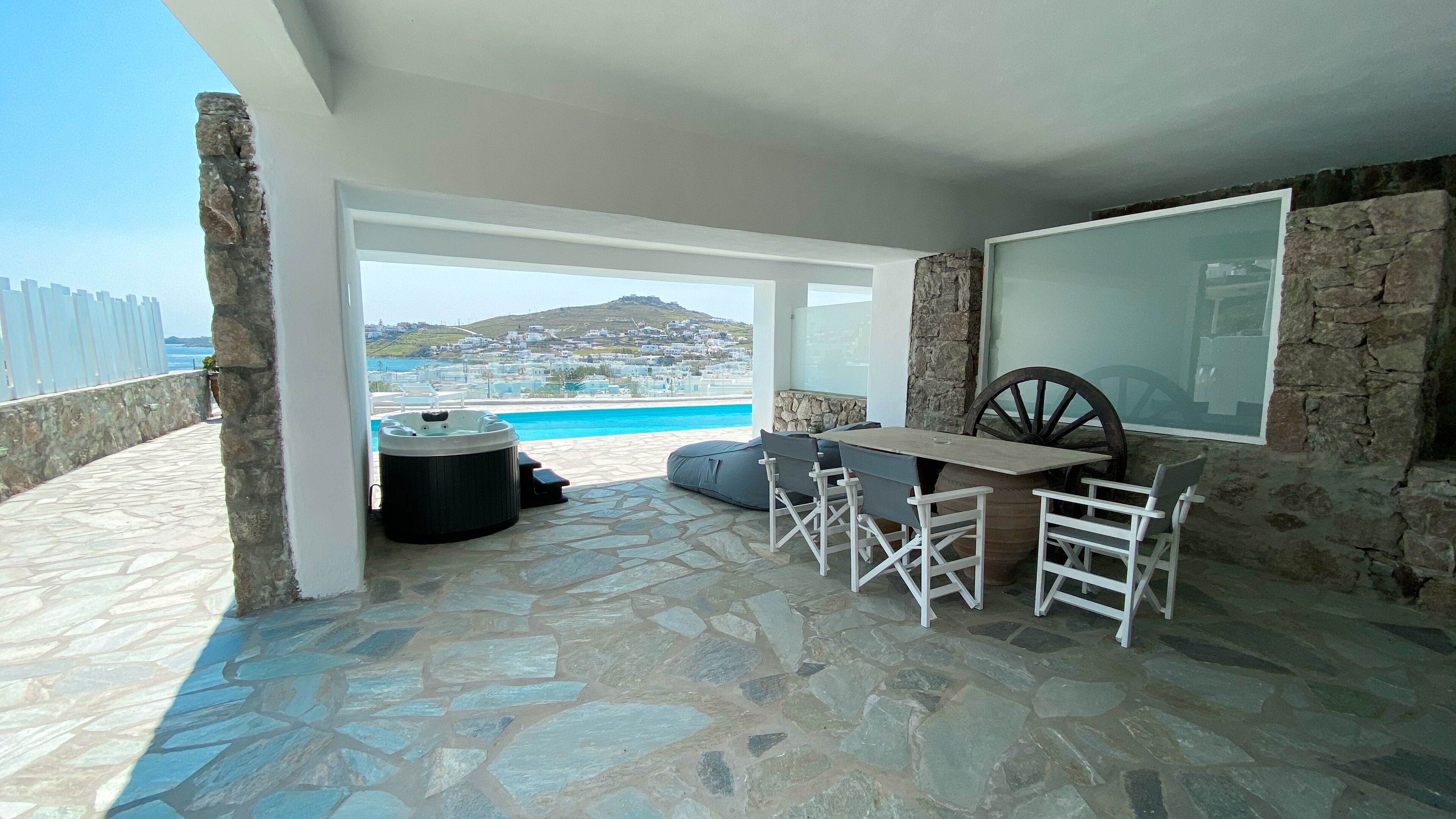 Une terrasse dallée de pierres, avec une table et des chaises, un jacuzzi et une vue sur une ville côtière et la mer.