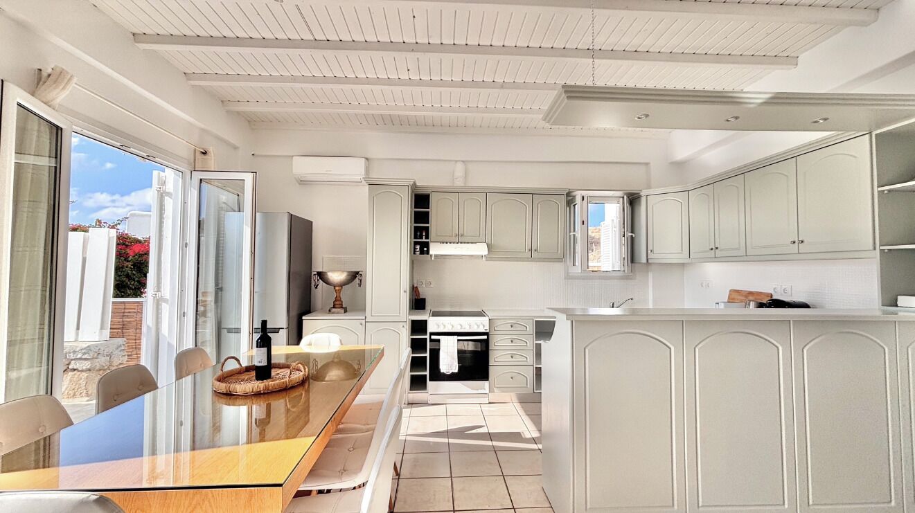 A modern kitchen with white cabinetry, a glass dining table, and a view of the outdoors.
