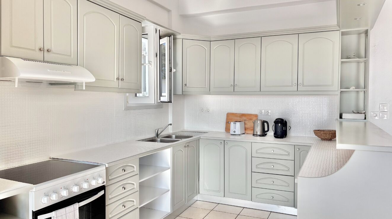 A modern kitchen with white cabinetry, a stove, a sink, and a coffee maker.