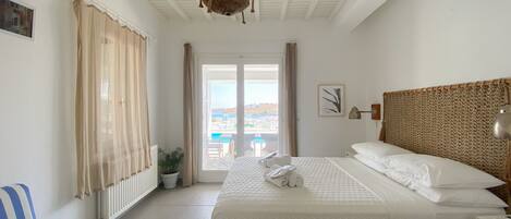 A bedroom with a bed, a nightstand, a lamp, a view of the sea, and a potted plant.