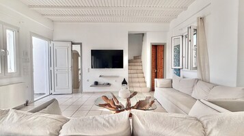 Una sala de estar moderna con un televisor grande, una escalera y una decoración en blanco.