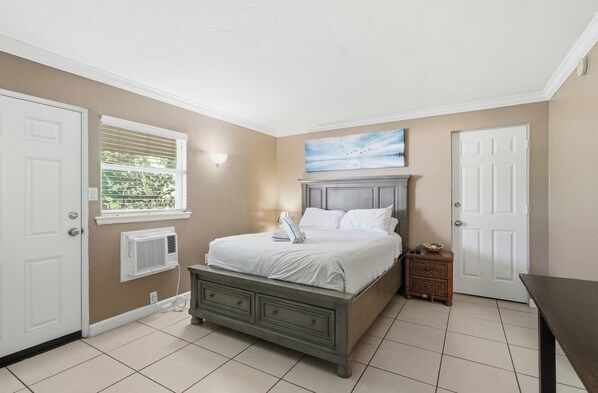 A bedroom with a bed, a window with blinds, a door, and a small table.