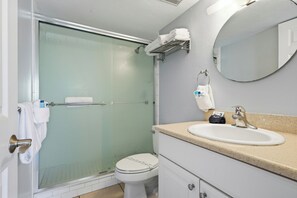 A bathroom with a glass-enclosed shower, a white toilet, a sink with a beige countertop, and a mirror above the sink.