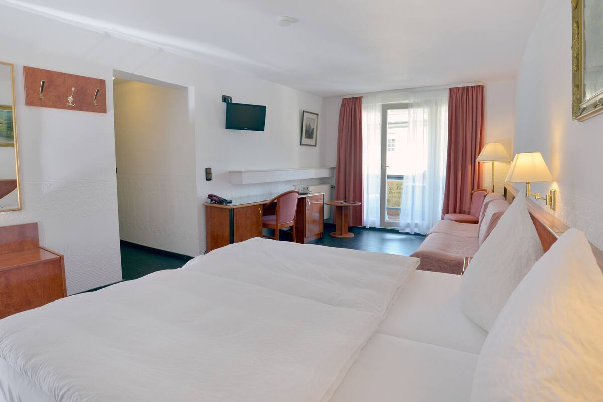 A hotel room with a large bed, a desk with a chair, a television, and a window with curtains.
