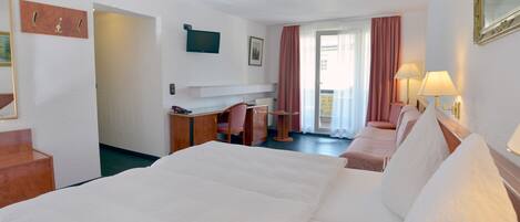Habitación de hotel con una cama grande, un escritorio con silla, televisión y ventana con cortinas.