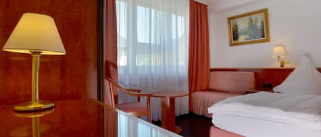 A hotel room with a bed, a chair, a small table, and a lamp.