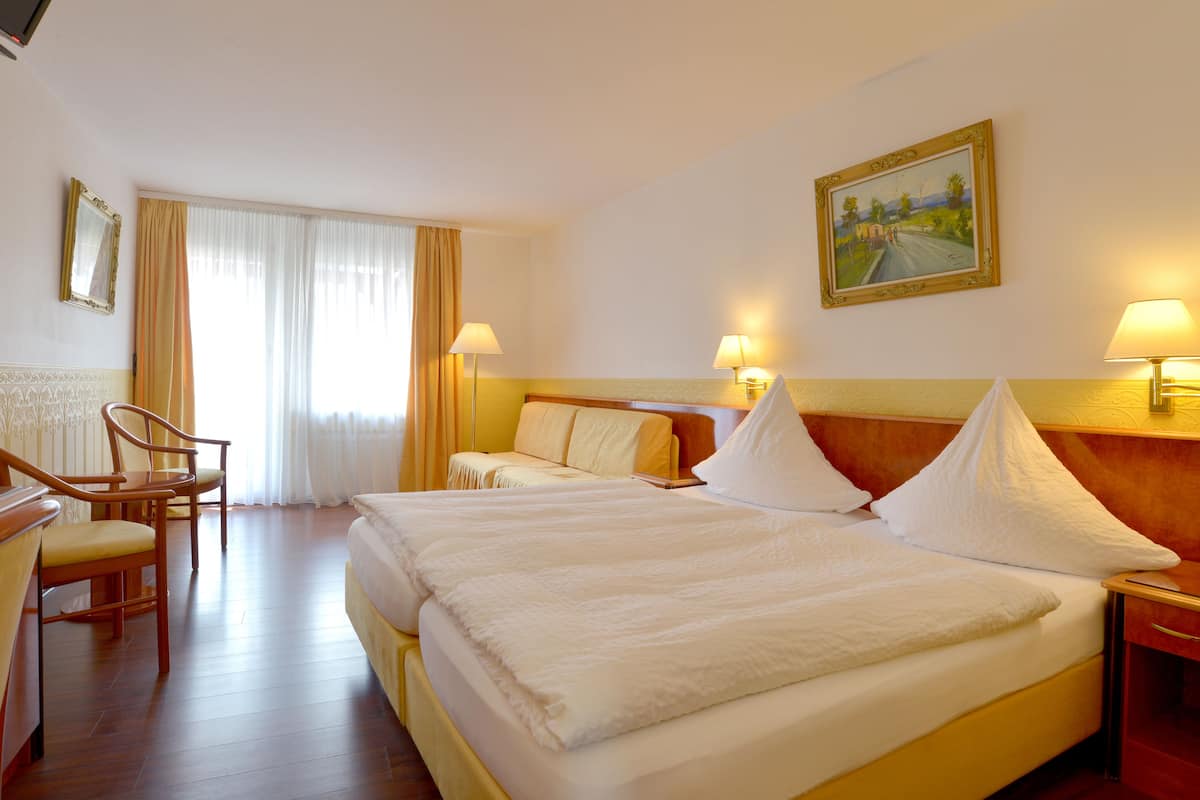 A hotel room with two beds, a desk, a chair, and a painting on the wall.