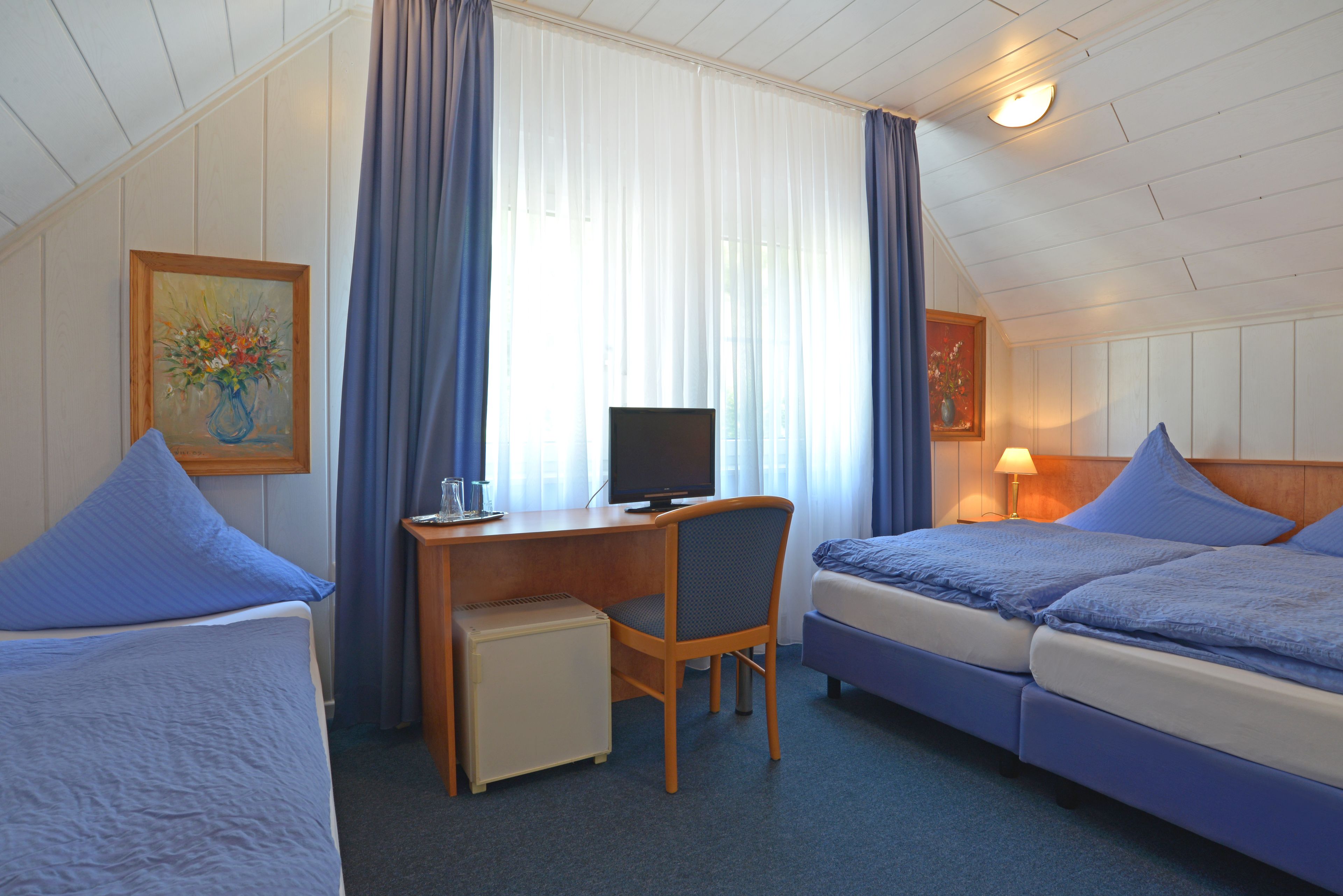 Una habitación de hotel con dos camas, un escritorio, una silla, un televisor y un refrigerador pequeño.