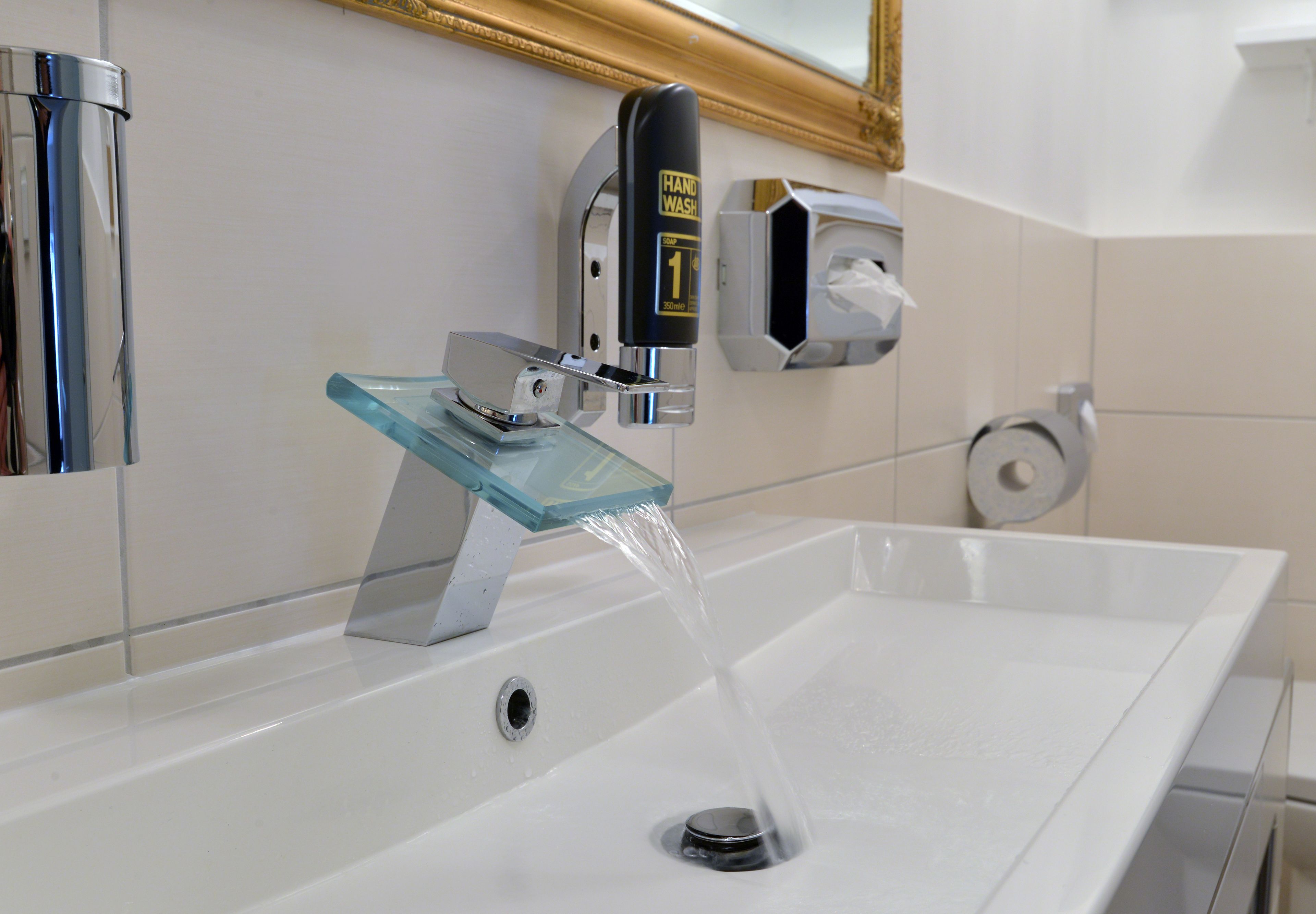 A modern bathroom with a glass sink, a hand wash station, and a toilet paper dispenser.