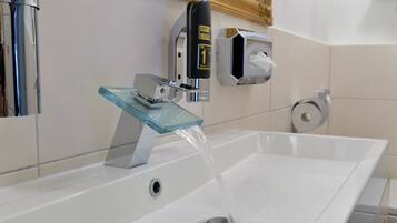 A modern bathroom with a glass sink, a hand wash station, and a toilet paper dispenser.