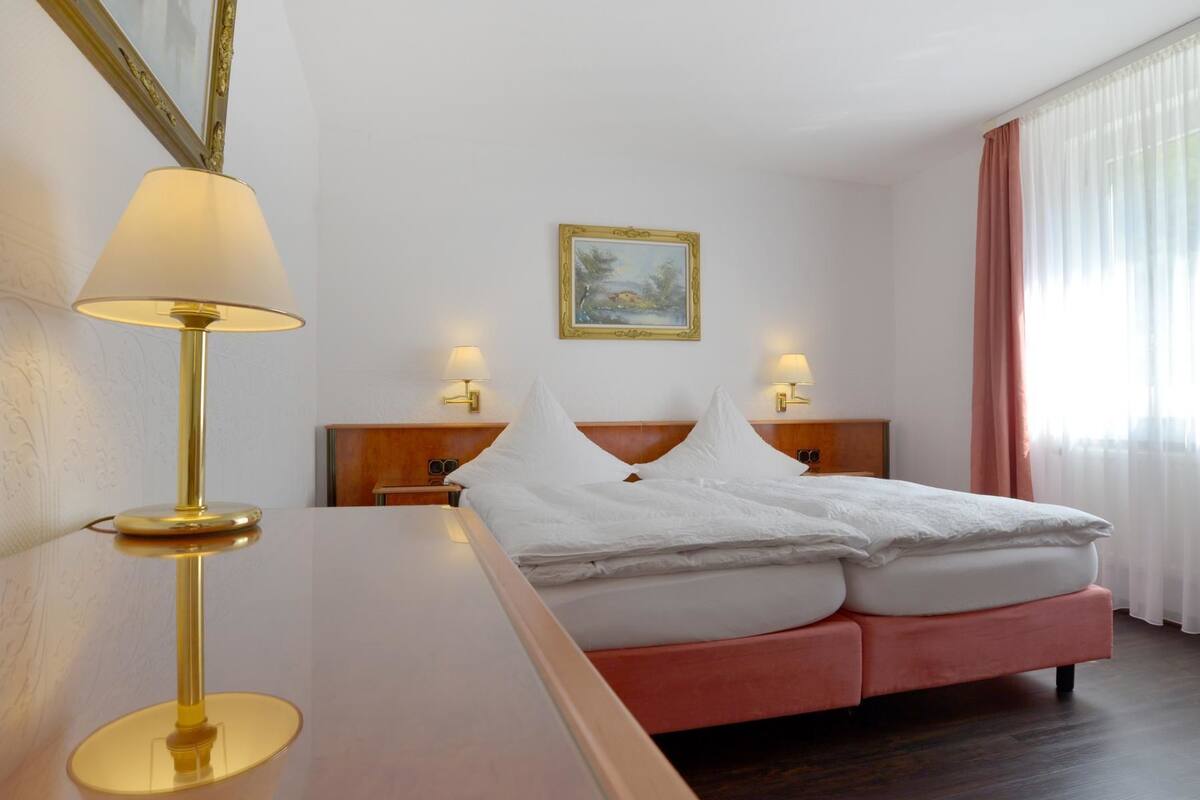 A hotel room with a bed, bedside lamps, a painting on the wall, and a window with curtains.