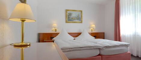 A hotel room with a bed, bedside lamps, a painting on the wall, and a window with curtains.