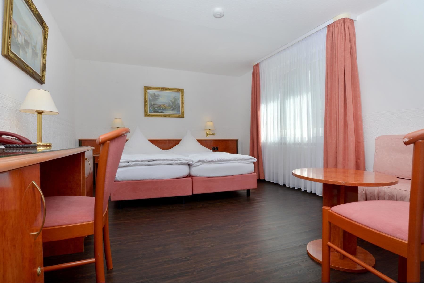 Een hotelkamer met een bed, een bureau met telefoon, een stoel, een klein tafeltje en een schilderij aan de muur.