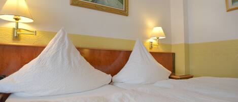 Una cama bien hecha con sábanas blancas y dos almohadas, un cabecero de madera y dos lámparas fijadas a la pared.