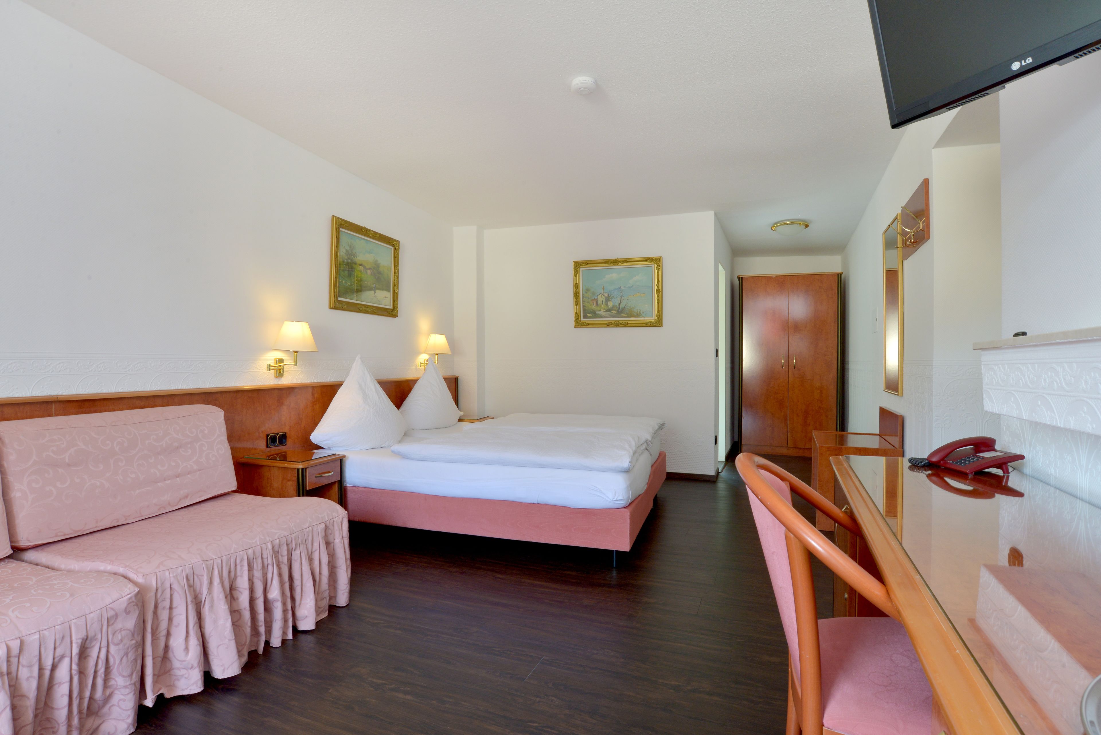 A hotel room with a bed, a sofa, a desk, a chair, a TV, and a door.