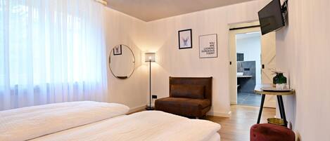 Une chambre d’hôtel avec deux lits, un lustre, un téléviseur à écran plat, un miroir rond et un pouf rouge.