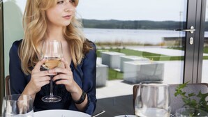 Iemand zit aan een tafel met een glas wijn, een bord eten en uitzicht op een meer.