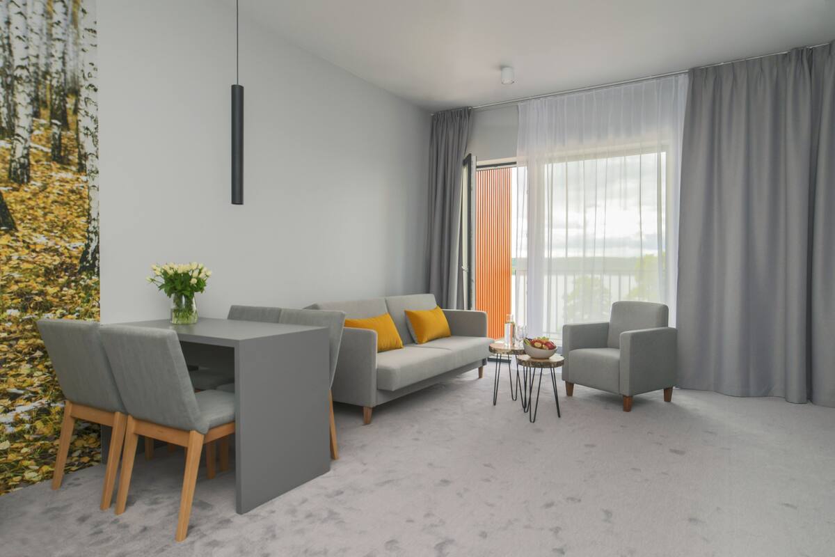 Una sala moderna con un sofá gris, dos sillones, una mesa de comedor con sillas y un ventanal con cortinas.