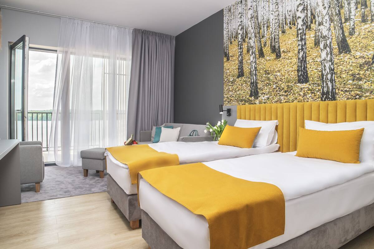 Habitación de hotel con dos camas, un escritorio, una silla y un balcón con cortinas.