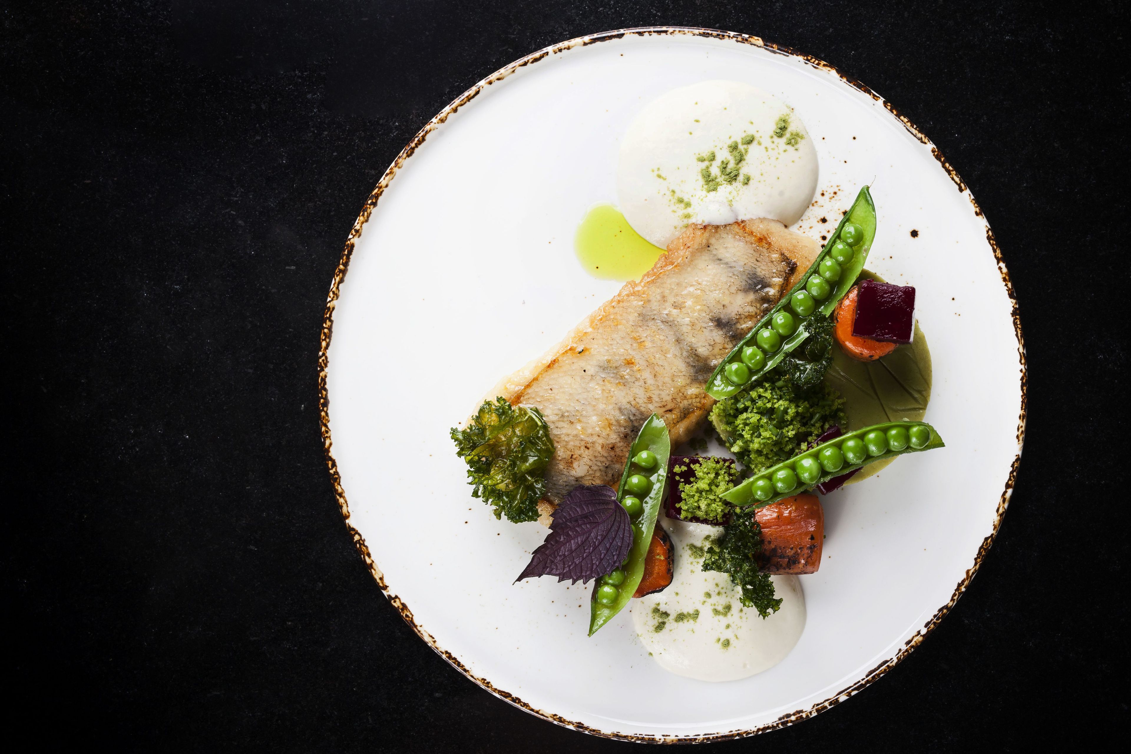Un piatto bianco con un pezzo di pesce, piselli, carote e broccoli.
