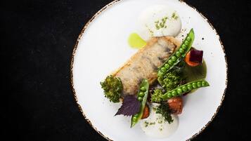 Un piatto bianco con un pezzo di pesce, piselli, carote e broccoli.