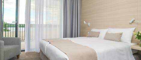 A modern hotel room with a large bed, a sitting area, and a balcony with a view.