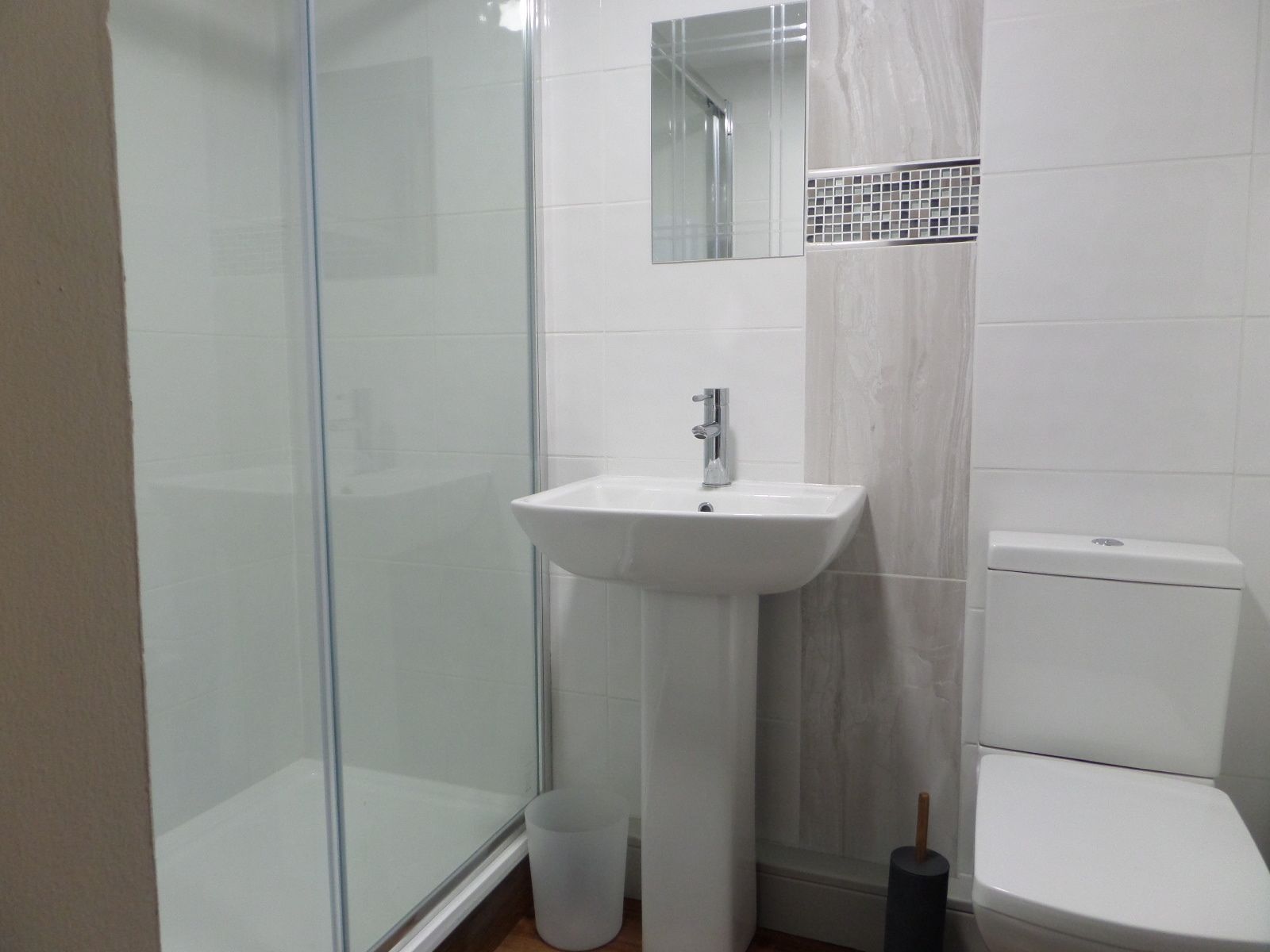 Ein Badezimmer mit Duschkabine aus Glas, einem weißen Waschbecken mit Spiegel darüber und einer Toilette.