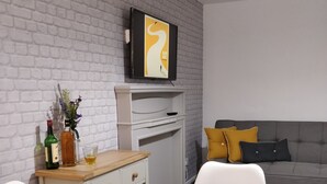 A modern living room with a white brick wall, a flat-screen TV mounted above a white console table, and a grey sofa with yellow cushions.