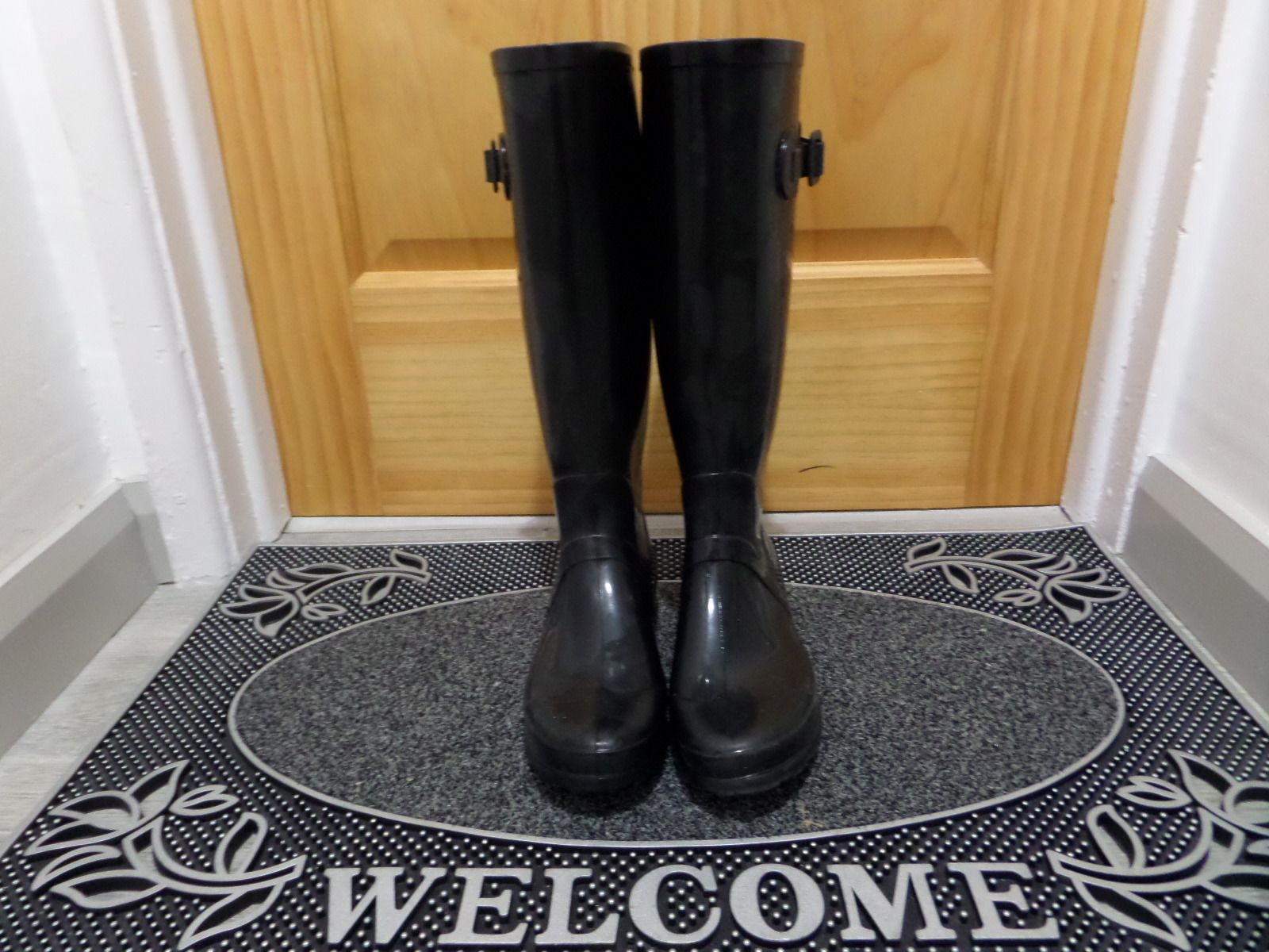 Un par de botas negras de pie sobre un felpudo con un diseño circular y la palabra 'WELCOME' en el centro.