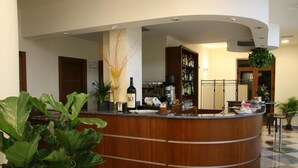 Zona de recepción con mostrador de madera curvada, cocina al fondo y plantas en macetas.