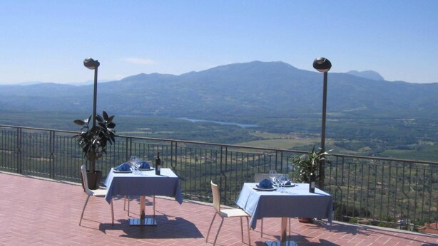 Una terraza con dos mesas dispuestas para comer, con vistas a un paisaje pintoresco con montañas y un valle.