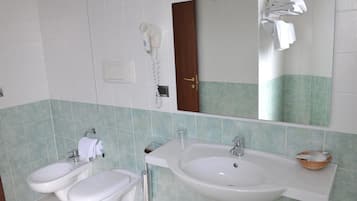 A bathroom with a large sink, two bidets, a toilet, a hairdryer, and a mirror.