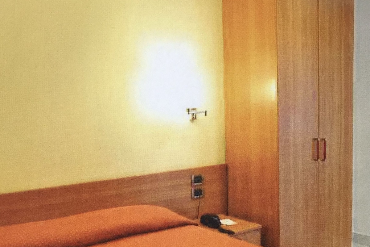 A hotel room with a single bed, a wooden wardrobe, and a bedside table with a telephone.