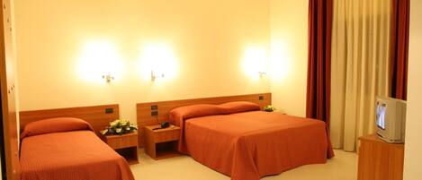 A hotel room with two beds, bedside tables, lamps, a TV, and curtains.