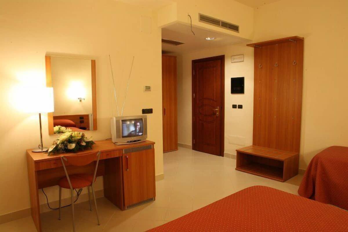 A hotel room with a wooden desk, a television, a chair, a bed, and a wardrobe.