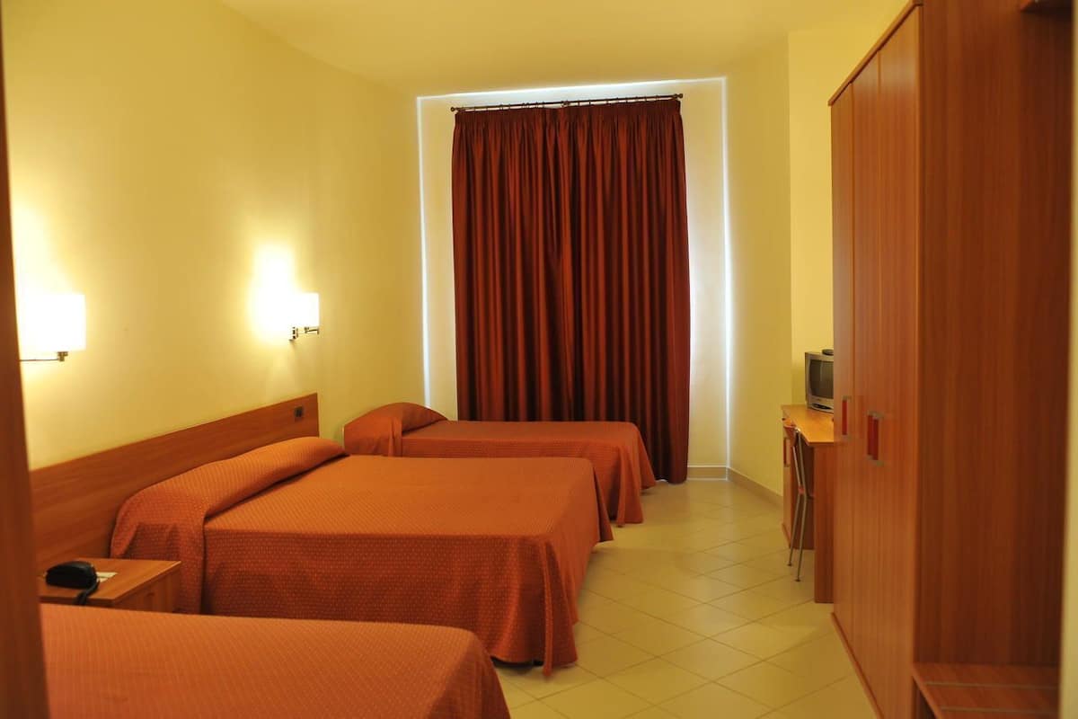 A hotel room with four beds, a television, a wardrobe, and a window with curtains.