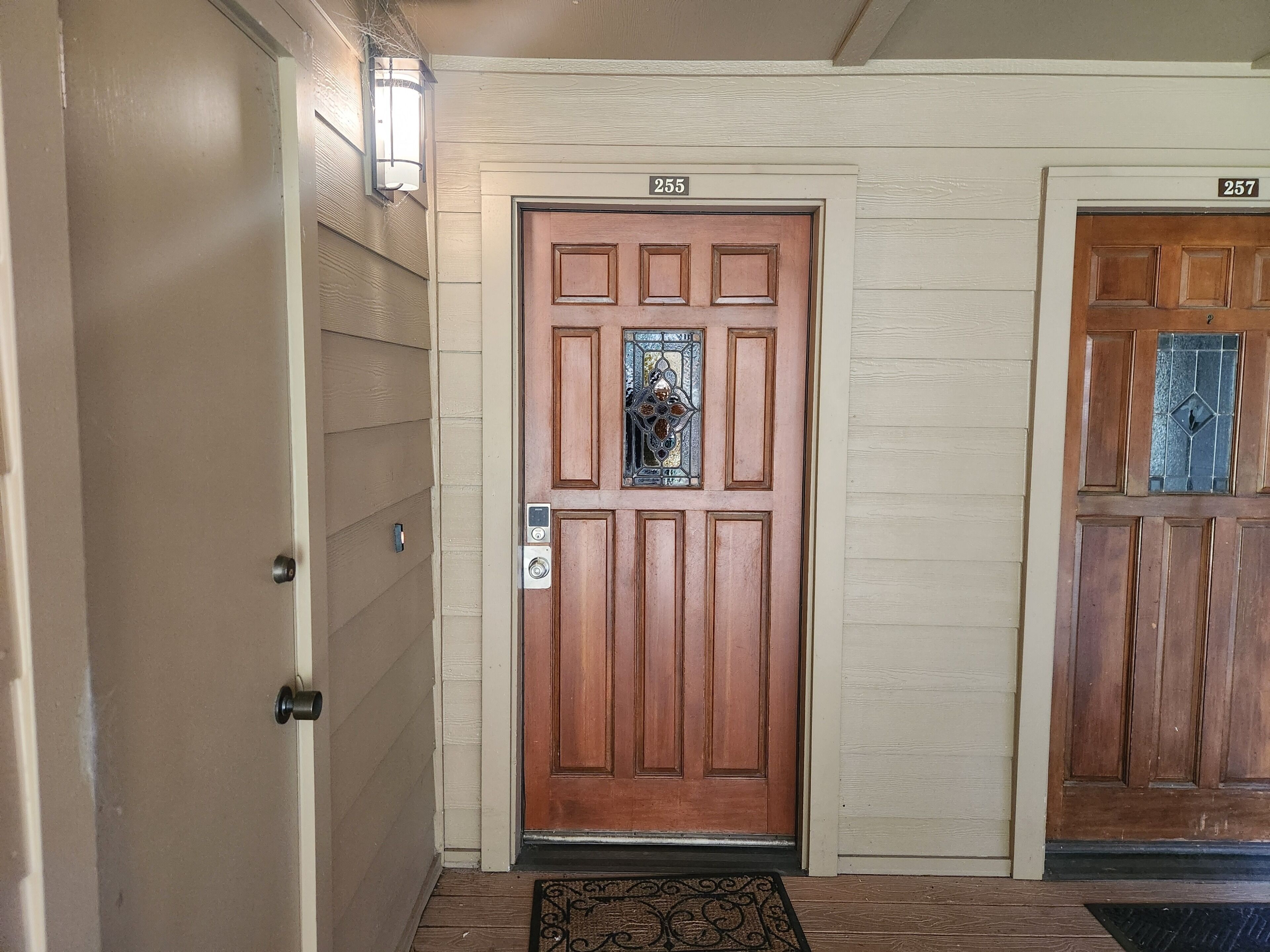 A wooden door with a number plate, a doormat, and a light fixture.