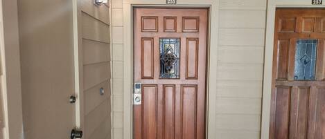 A wooden door with a number plate, a doormat, and a light fixture.