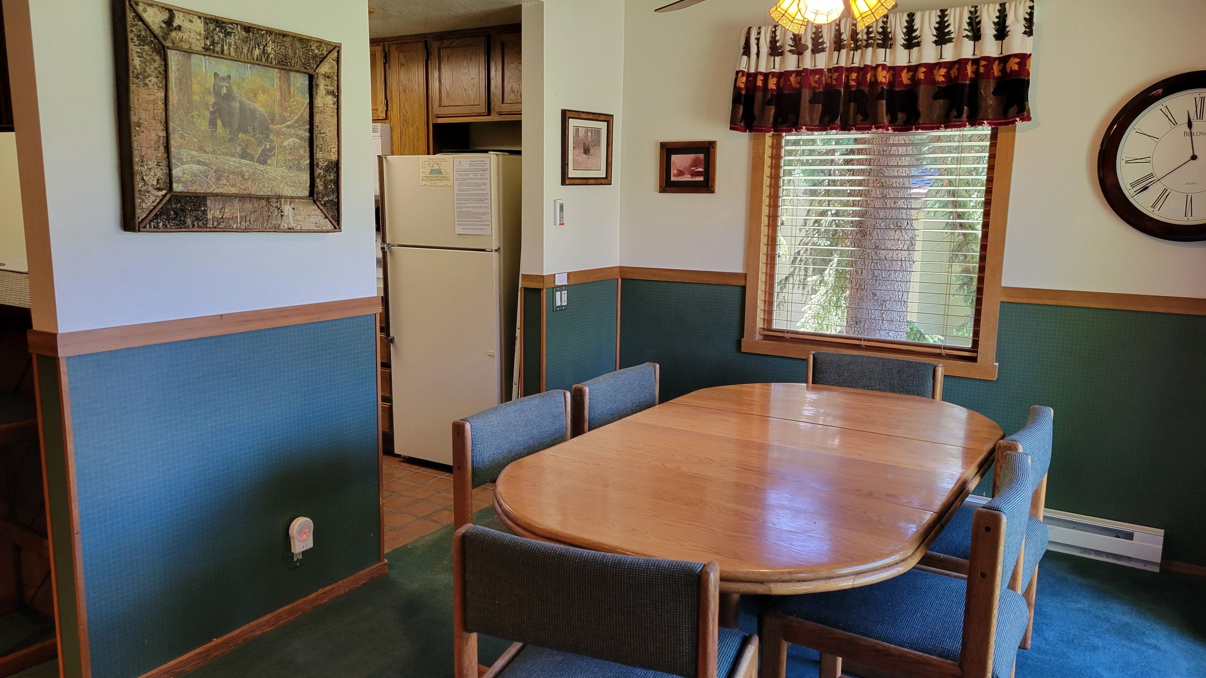 Un comedor con una mesa y sillas de madera, un refrigerador y un reloj en la pared.