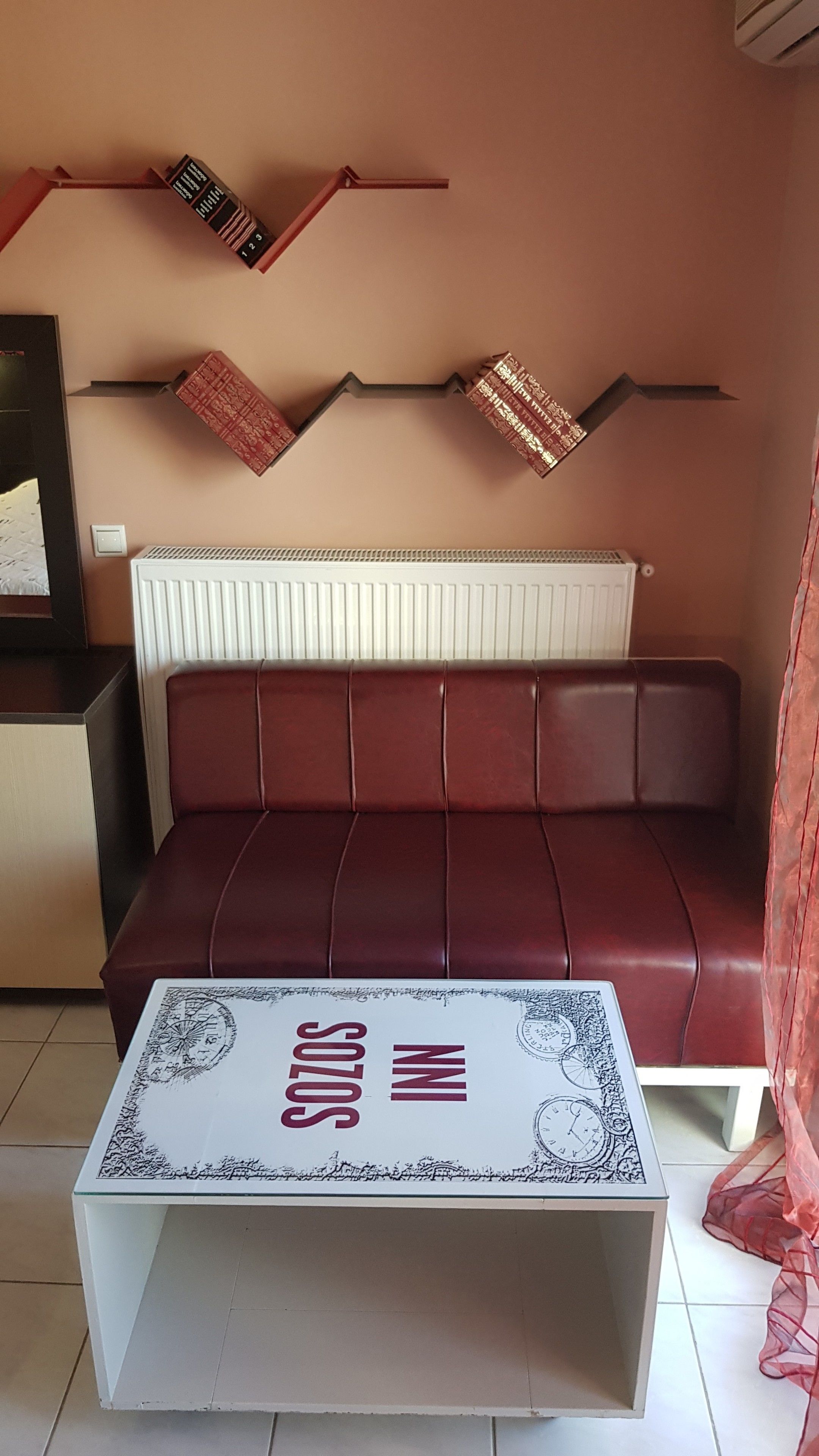 A living room with a red leather sofa, a white coffee table with a patterned top, and decorative items on the wall.