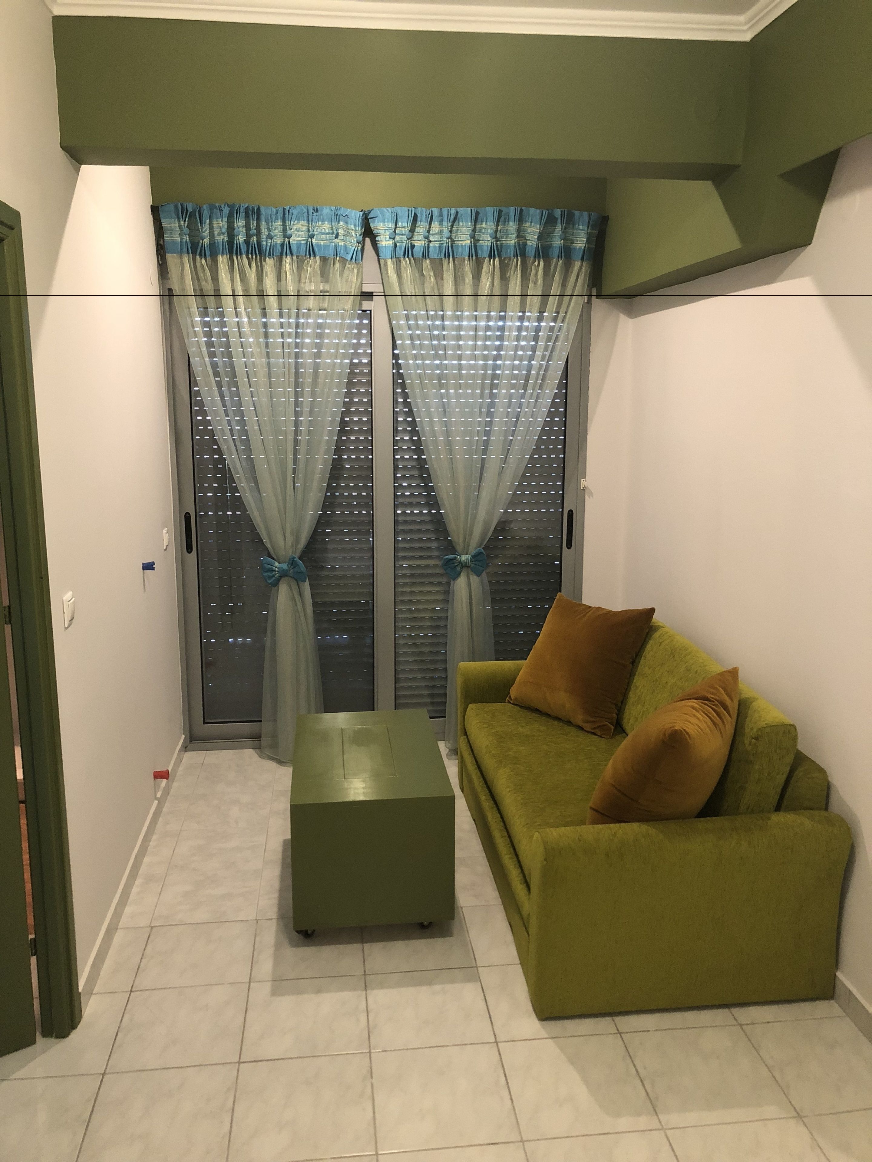 Een kamer met een groene bank, een passende voetenbankje en een raam met dunne gordijnen.