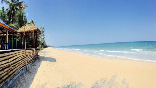 A beach with a thatched-roof structure, palm trees, and a clear blue sky. - Kasemsuk Resort (Bang Saphan)
