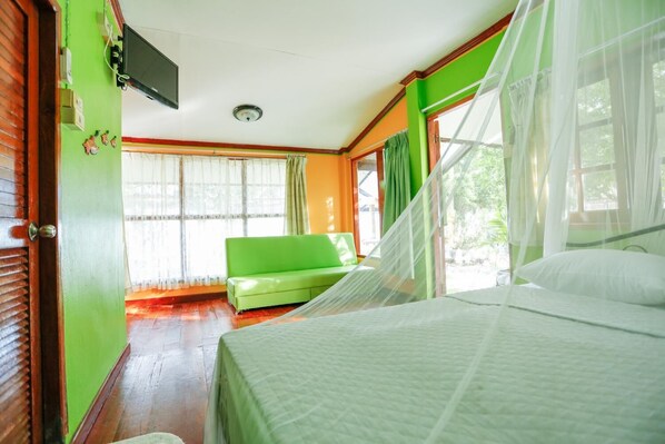 A room with a bed, a green sofa, a television on the wall, and a window with curtains.